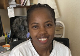 Joyce from Kenya is sitting in an office chair, smiling.