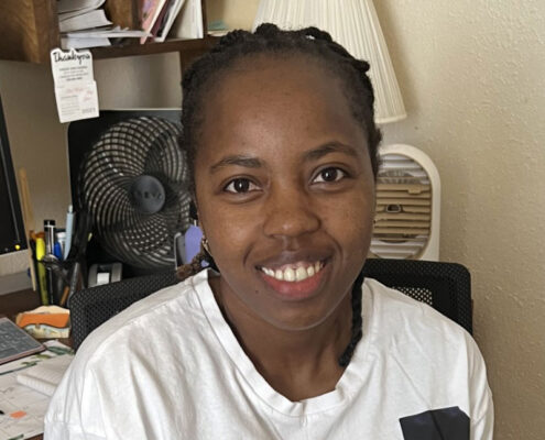 Joyce from Kenya is sitting in an office chair, smiling.