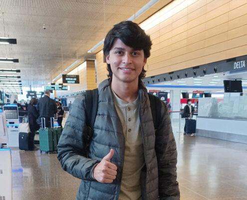 Pedro from Venezuela is in an airport smiling and giving the thumbs up sign with his right hand.