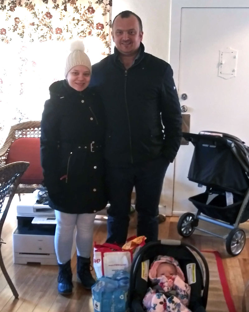 Dmitry and family from Ukraine are standing in an office with their young baby in a car seat and a few small bags.